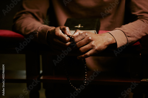 Hands of unrecognizable Black man holding rosary praying in Catholic church, copy space