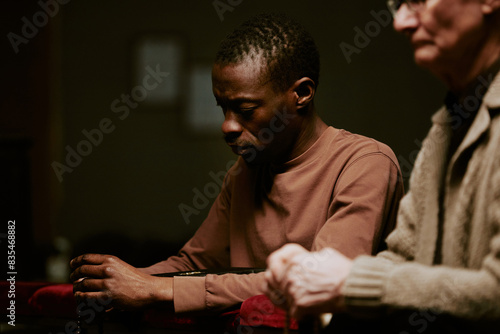 Selective focus shot of senior Caucasian and young Black men holding rosary praying during service in Catholic church