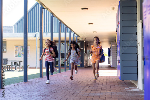Three biracial girls are running joyfully down a school corridor