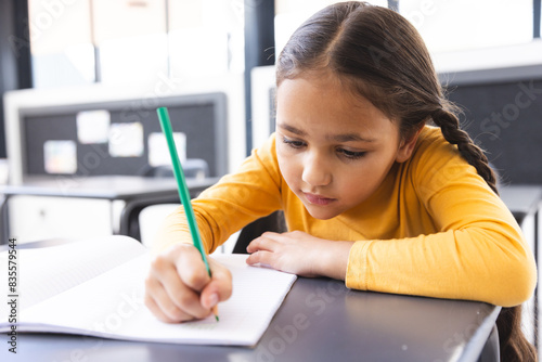 In school, young biracial girl with light brown skin focusing on writing in the classroom