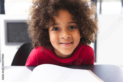 In school, young biracial male student wearing a red shirt reading a book in the classroom
