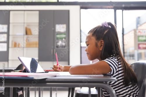 In school, young biracial girl focusing on her tablet in the classroom with copy space