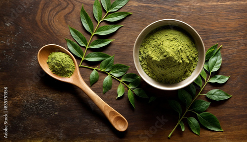 A wooden spoon with green henna powder or in it sits next to a bowl of green powder and green leaves