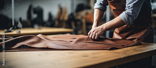 Craftsman with a warm smile, wearing an apron, holds tanned leather rolls in a leather craft workshop, creating a visually appealing copy space image.