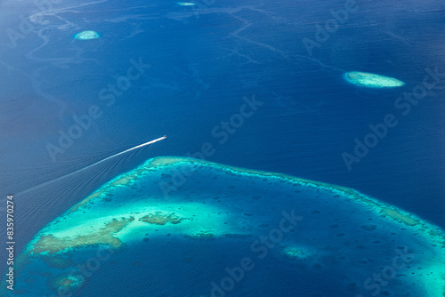 Maldives islands beach with speed boat passing from birds eye view. Aerial view on Maldives island Ari atoll. Tropical islands and atolls from aerial view. Summer tourism background. Wanderlust travel