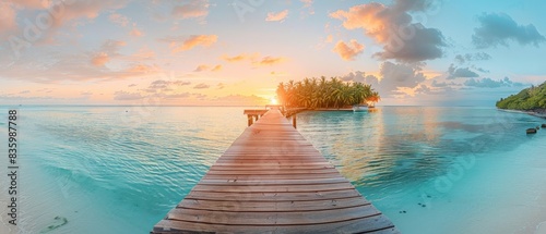 The photo shows a beautiful beach with a wooden dock jutting out into the calm water. The sky is a gradient of orange and yellow, and the sun is setting over the horizon.