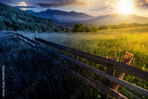 wooden fence across the grassy rural field at summer solstice. mountainous countryside scenery beneath a sky with sun and moon. day and night time change concept