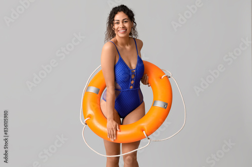 Beautiful young African-American woman in stylish blue swimsuit with lifebuoy on grey background