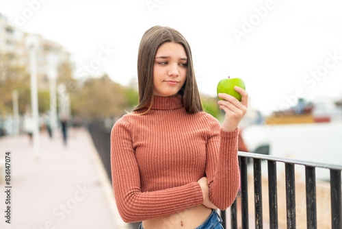 Teenager girl with an apple at outdoors with sad expression