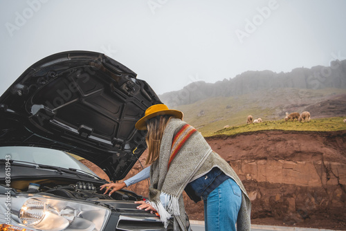 A woman in a yellow hat is standing next to a car with the hood up, tourist in the peruvian andes