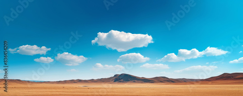 Vast desert landscape with mountains under a bright blue sky and scattered clouds. Nature and wilderness concept