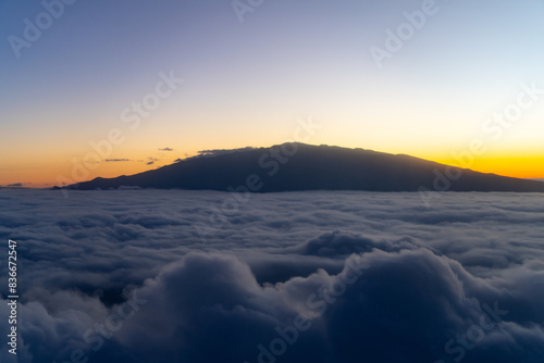 Aerial photo of Mauna Loa and Mauna Kea above the clouds at sunset. Flight from Hilo to Honolulu.