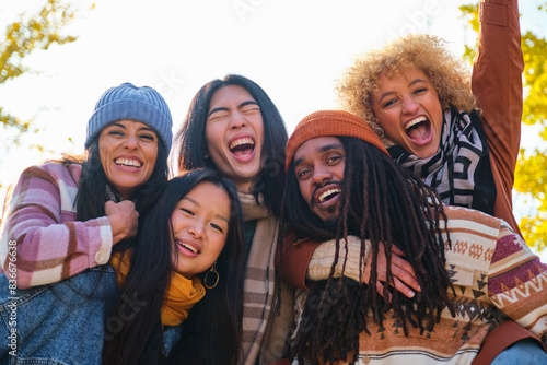 Multiethnic friends having fun walking on city street in autumn. Group of young people enjoying together outdoors. Friendship concept with guys and girls hanging outside on a sunny day of fall.