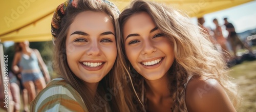 Two cheerful young women capturing a selfie at a campsite during a lively summer music festival with a background perfect for a copy space image.