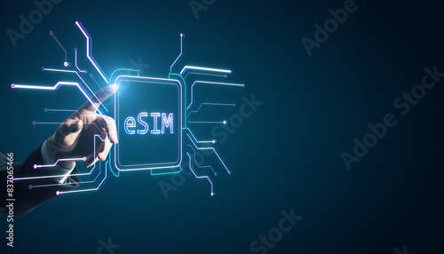 Close up of businessman hand pointing at creative glowing eSim hologram on blurry background with mock up place. Embedded sim and cellular mobile technology concept.