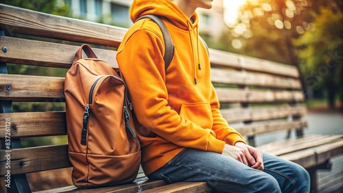 Close up of a young man's orange hoodie and backpack on a wooden bench