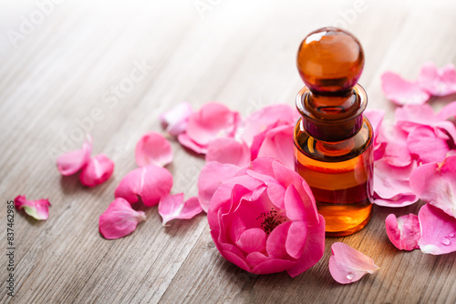 roses essential oil, fragrant pink rose, a heap of delicate petals and essential oil in an old-fashioned amber glass apothecary bottle on a wooden background, perfume, natural cosmetics design element