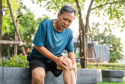 Mature man tired and leg pain during jogging at nature park. Runner has sore knees because he has been running for too long. Exercising until the injury. Training athlete work out at outdoor.