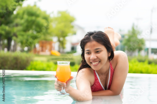 Young woman in bikini and hat in swimsuit laying on chaise-longue and sunbathing by the pool in a summer vacation