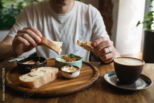 Close-up of man eating breakfast with sausages, cauliflower fritters, bread, butter with a cup of coffee. 