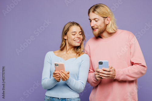 Young happy couple two friends family man woman wear pink blue casual clothes together hold in hand use looking at mobile cell phone isolated on pastel plain light purple background studio portrait.