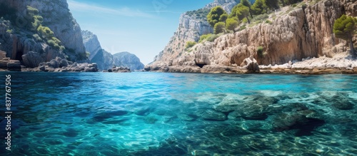 A scenic Mediterranean cove with crystal clear blue waters, surrounded by cliffs, featuring visible stones on the seabed; ideal for a copy space image.