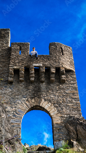 portrait of latin man sitting pose and smiling at the camera on balcony in historical castle location with blue sky. Vertical photo