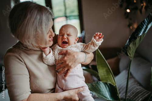 Grandmother holding crying baby girl in arms, calming her down, soothing her. Strong bond between grandparent and grandchild.