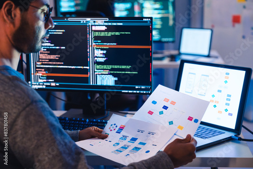 Indian software development working on coding computer screen and flowchart at night in modern office