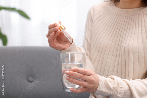 Woman dripping food supplement into glass of water indoors, closeup. Space for text