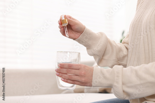 Woman dripping food supplement into glass of water indoors, closeup. Space for text