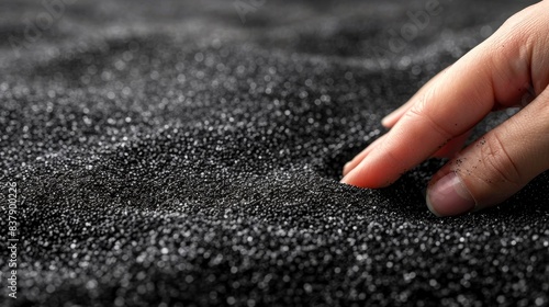 Close-up of a hand touching a black granular texture, creating subtle waves. Ideal for concepts of texture, sensory perception, and fine detail.