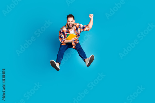 Full length portrait of nice young man jump raise fist wear shirt isolated on blue color background