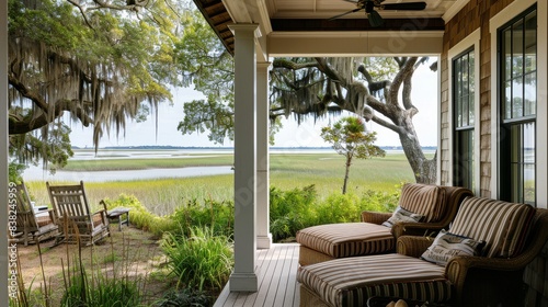 Charming covered porch with striped chairs and ottoman overlooking scenic marshland and Morris Island in Beaumont, South Carolina. Wood-paneled walls and white ceiling with large windows open to ocean