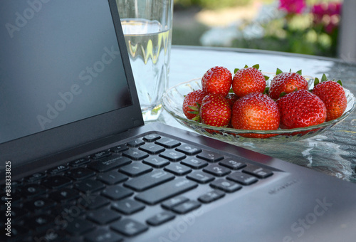 home office w ogrodzie, praca przy komputerze w ogrodzie, laptop. truskawki i woda na stoliku w ogrodzie w słonecnzy dzień, home office in the garden, laptop, strawberries and water on a table