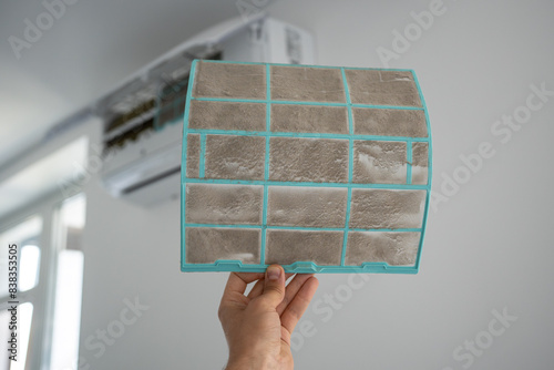 Person removing dirty dusty air conditioner coarse filter for washing, cleaning. Home air conditioner service maintenance, repair and clean equipment. Dust - cause of illness. Closeup.