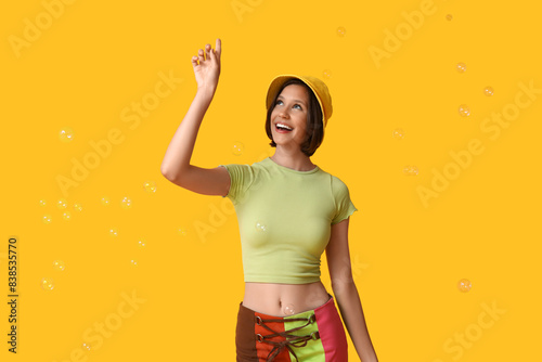 Teenage girl blowing soap bubbles on yellow background