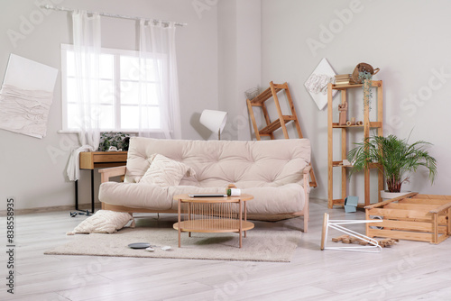 Interior of messy living room with sofa, tables and shelf units