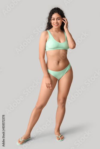 Beautiful young African-American woman in stylish turquoise swimsuit on grey background