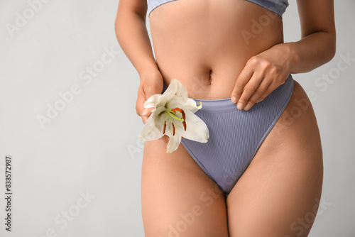 Beautiful young African-American woman in panties with white lily flower on grey background, closeup