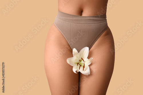 Beautiful young African-American woman in panties with white lily flower on beige background, closeup