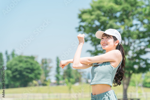 公園でストレッチ・準備体操・ウォーミングアップするスポーツウェア姿の若いアジア人女性 