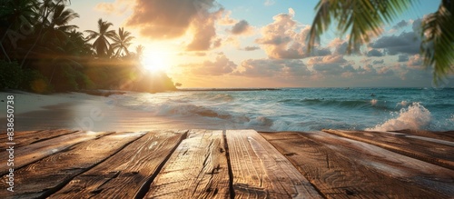A beautiful beach scene with a wooden boardwalk and a body of water. The sun is setting, casting a warm glow over the scene. The water is calm, and the sky is filled with clouds, creating a serene