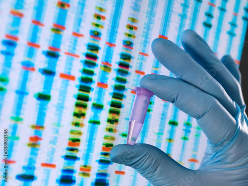 Scientist holding a DNA sample with the results on a computer sceeen in a laboratory