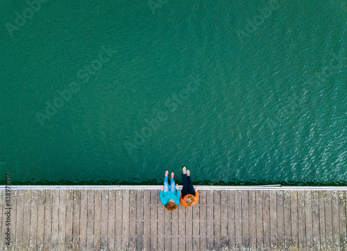 Two friends sitting side by side on jetty, Valdemurio Reservoir, Asturias, Spain