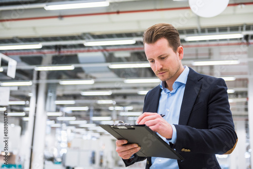 Man standing in factory shop floor taking notes