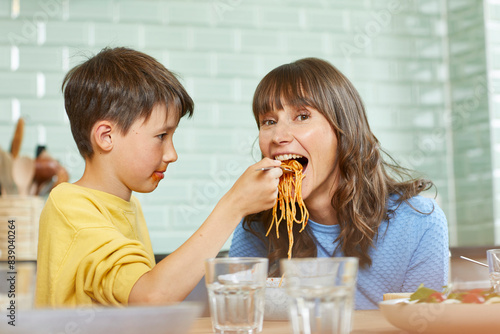 Son feeding mother with spaghetti in the kitchen