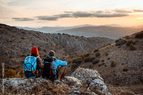 Male and female hikers enjoying sunset while sitting on rock mountain during vacation