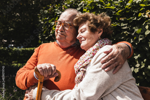 Senior couple sitting on bench in a park, with arms around