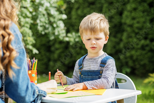 Focused child drawing with babysitter outside. Early years. Baby development.